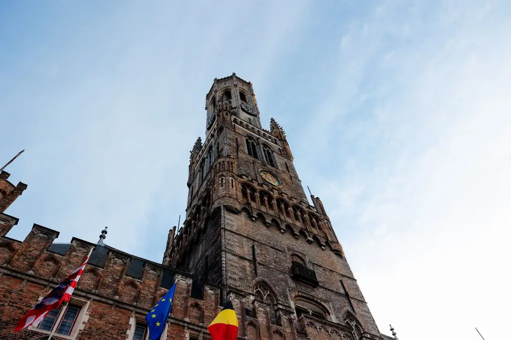 Stunning low-angle view of the Belfry of Bruges tower with clear sky and flags.