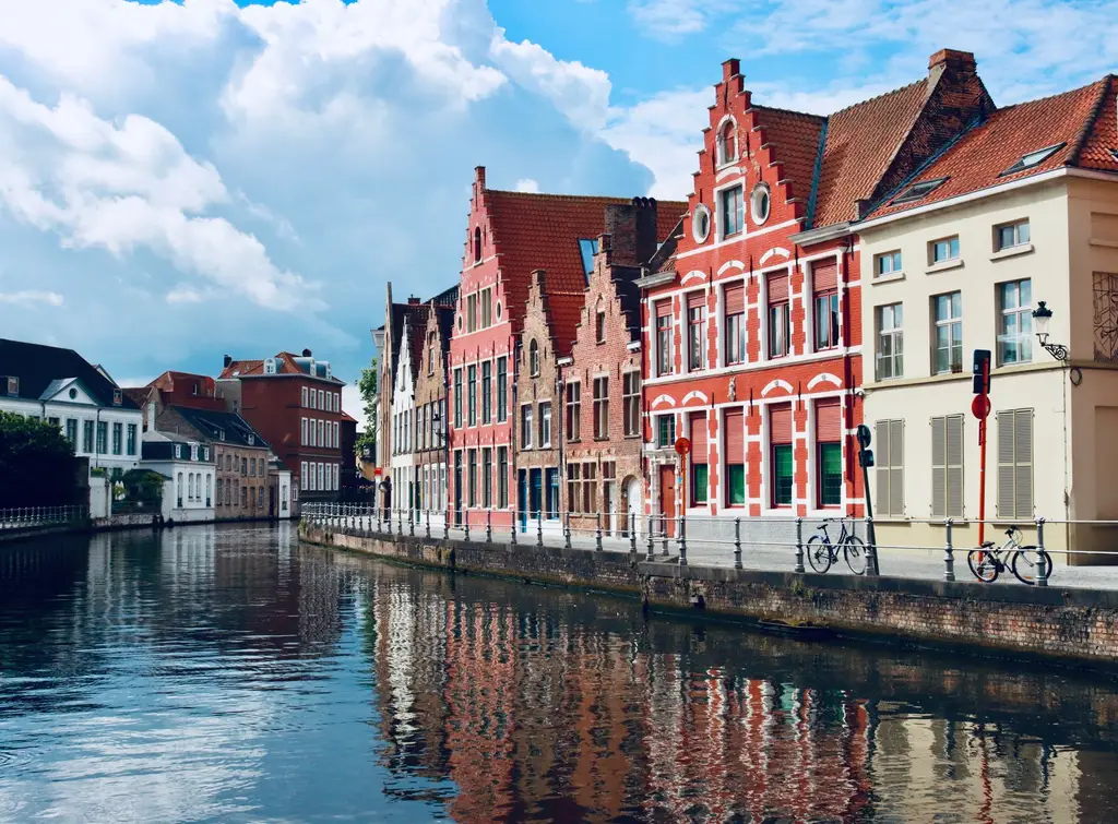 Picturesque canal-side houses reflecting in the water in Bruges, Belgium, under a blue sky.