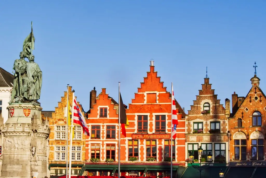 Colorful Flemish buildings in Bruges' Markt Square during a sunny day.