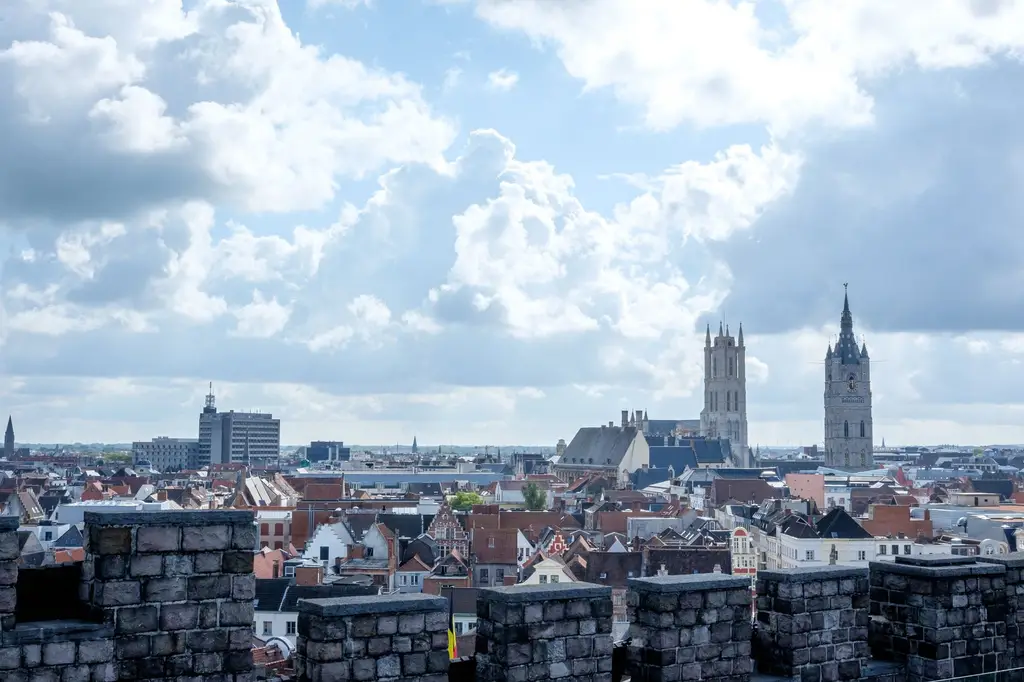 A wide view of Ghent showcasing Gravensteen Castle and church spires under a cloudy sky.