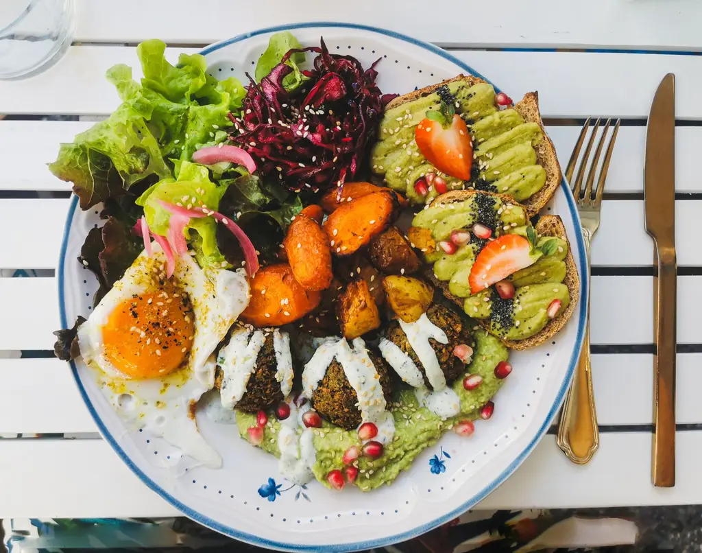 A vibrant vegan brunch plate featuring fresh salad, falafel, avocado toast, and roasted vegetables.