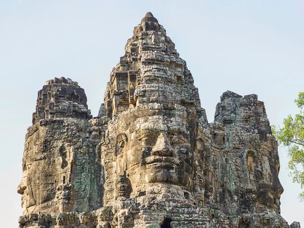 Intricate stone carvings of Bayon Temple in Angkor Thom, Cambodia under a clear sky.