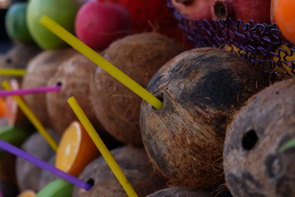 Vibrant close-up of coconuts with colorful straws at a tropical market, highlighting fresh fruit.