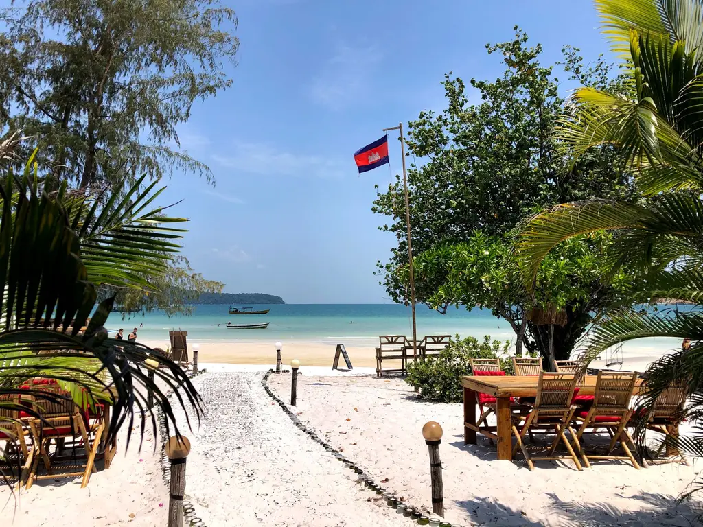 Beachfront dining area with palm trees and Cambodian flag in Sihanoukville.