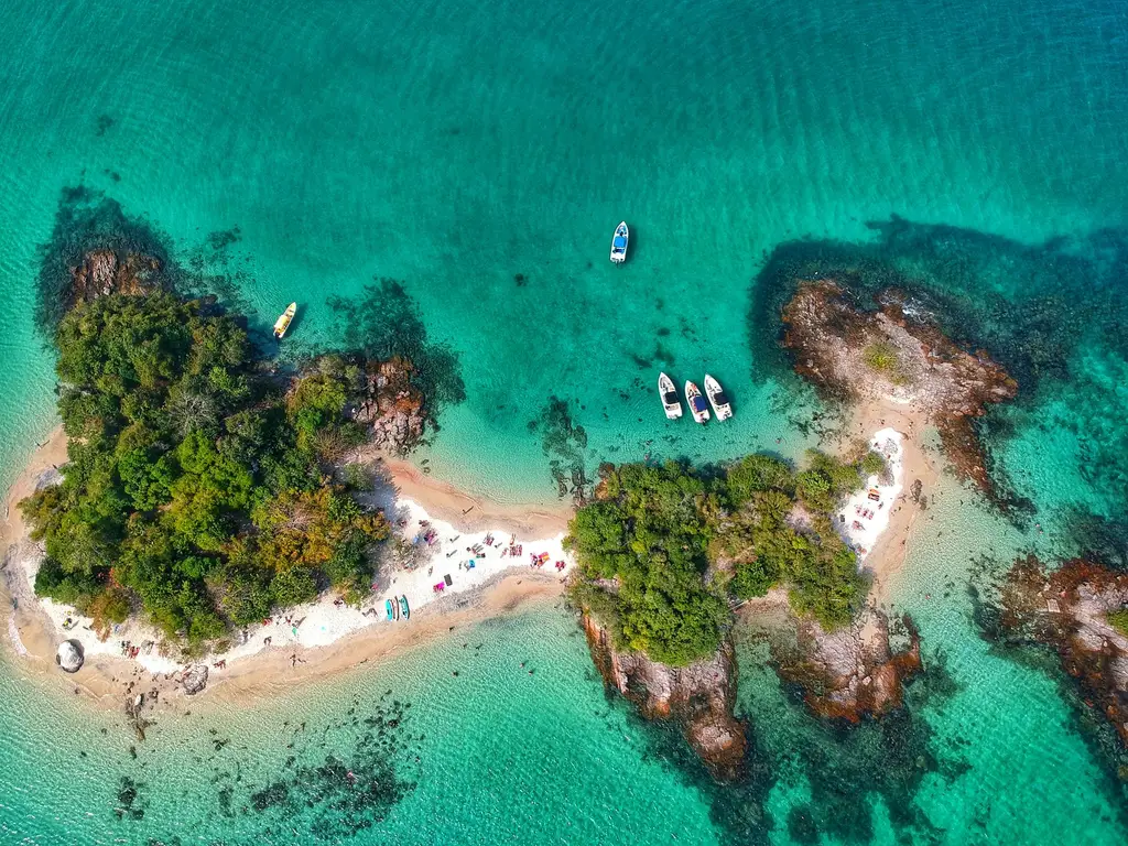 Breathtaking drone view of picturesque island with lush green trees in turquoise ocean with floating yachts on sunny day