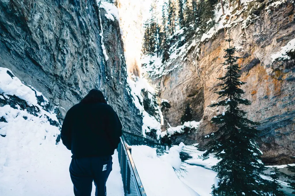A person hiking through snow-covered Johnston Canyon in Banff National Park during winter.
