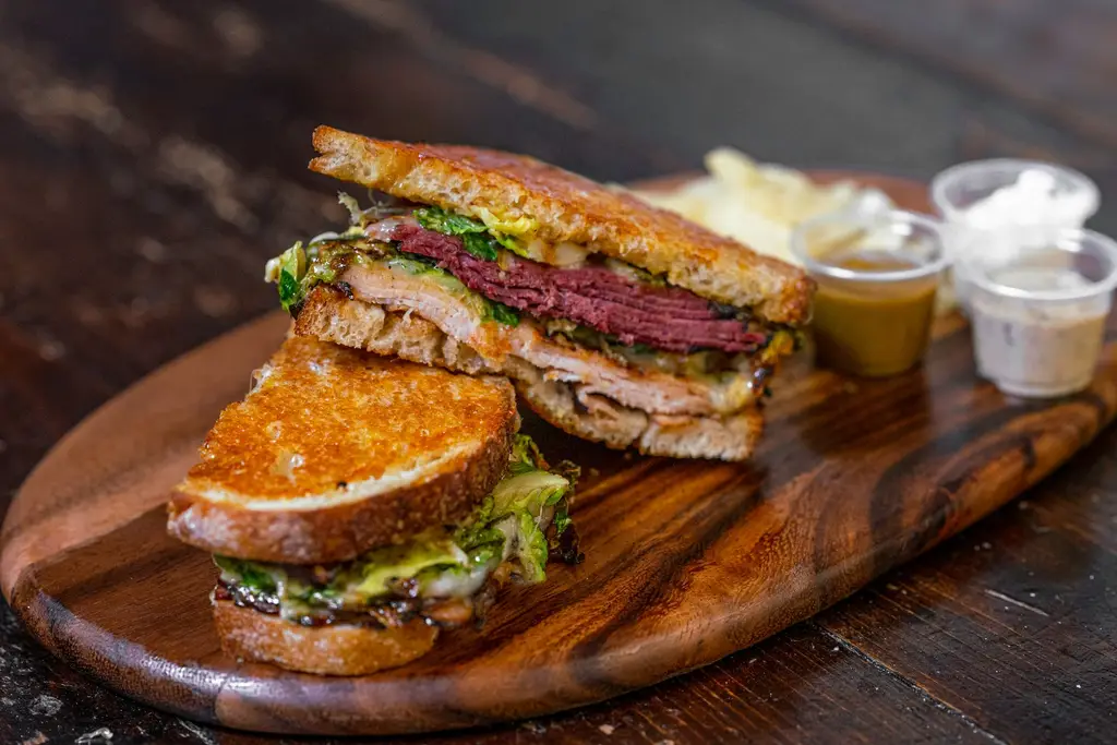 Delicious gourmet sandwich with layers of meats and vegetables on a wooden cutting board.