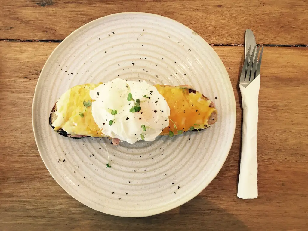 Tasty breakfast featuring poached egg on melted cheese toast, served on rustic plate.