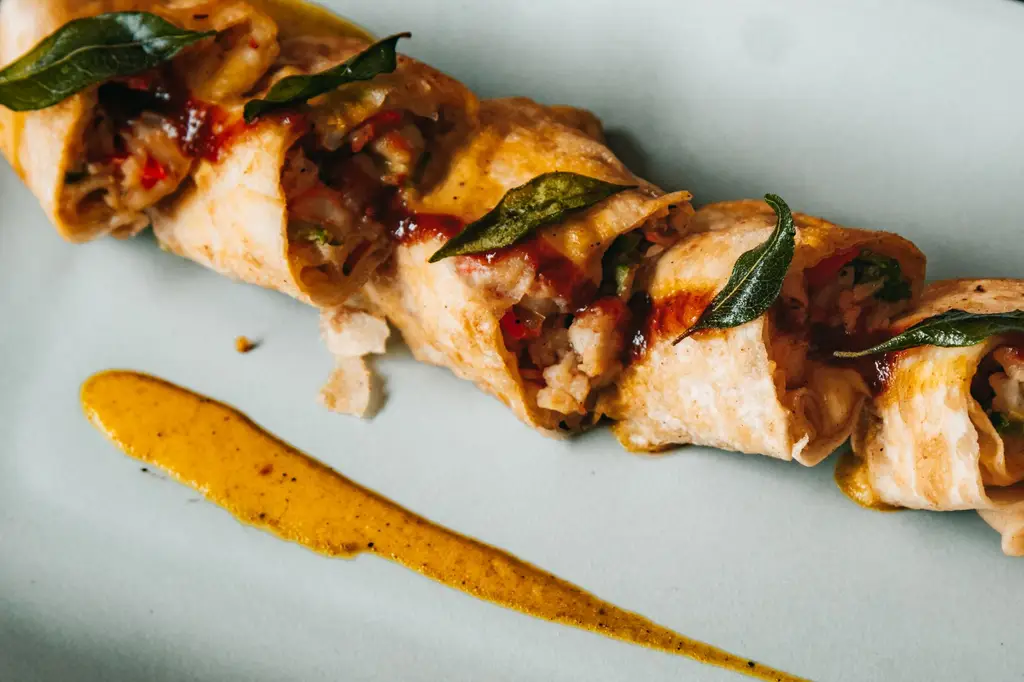 Close-up of a savory stuffed wrap with curry sauce, topped with fresh herbs.