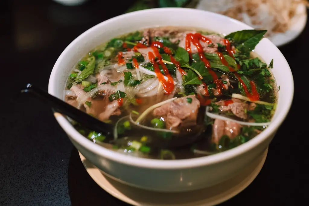 Delicious bowl of traditional Vietnamese pho garnished with fresh herbs and spicy sauce.