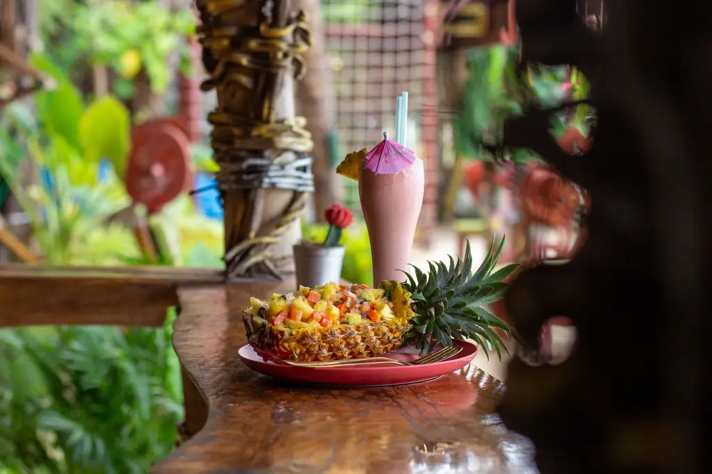 A vibrant tropical fruit salad served in a pineapple with a refreshing smoothie, perfect for summer vibes.