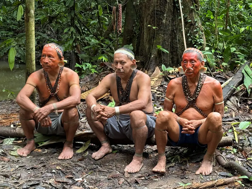 Three indigenous elders sitting in the Amazon rainforest, showcasing traditional attire and customs.
