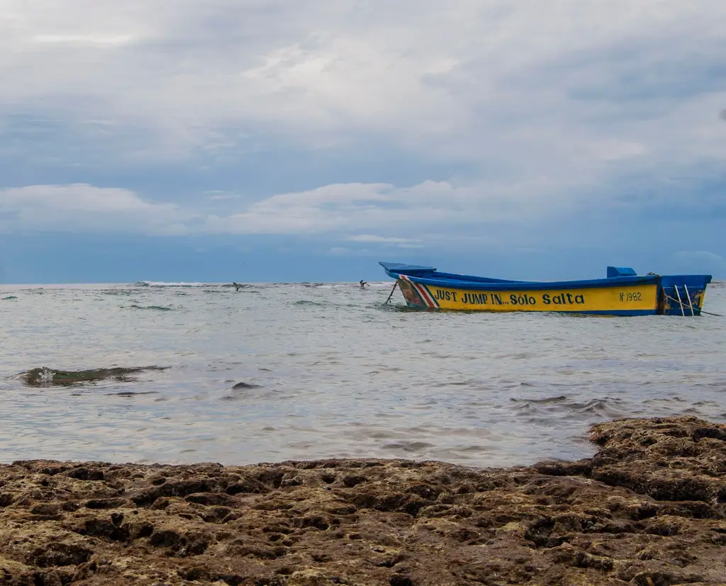 Vibrant boat on the serene shores of Puerto Viejo, Costa Rica, with rocky foreground.