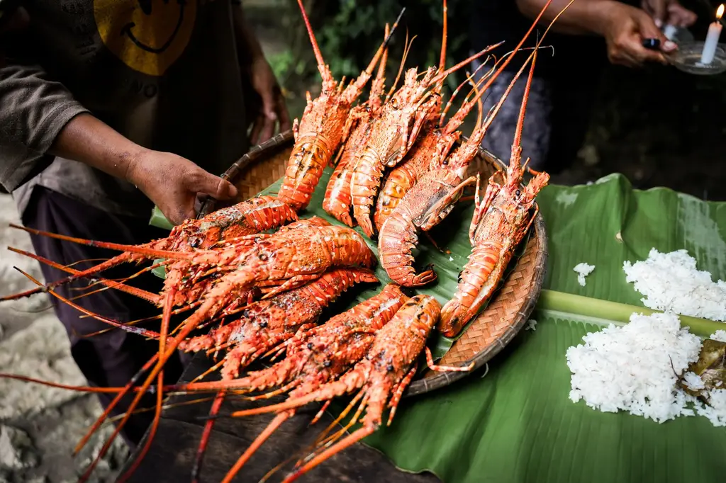 A basket of grilled lobsters served on banana leaves with rice outdoors.