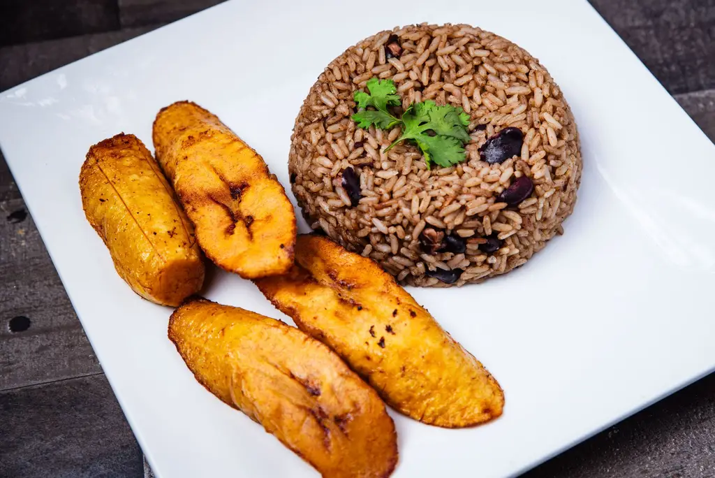 A savory plate of rice and beans with fried plantains on a white plate, garnished with parsley.
