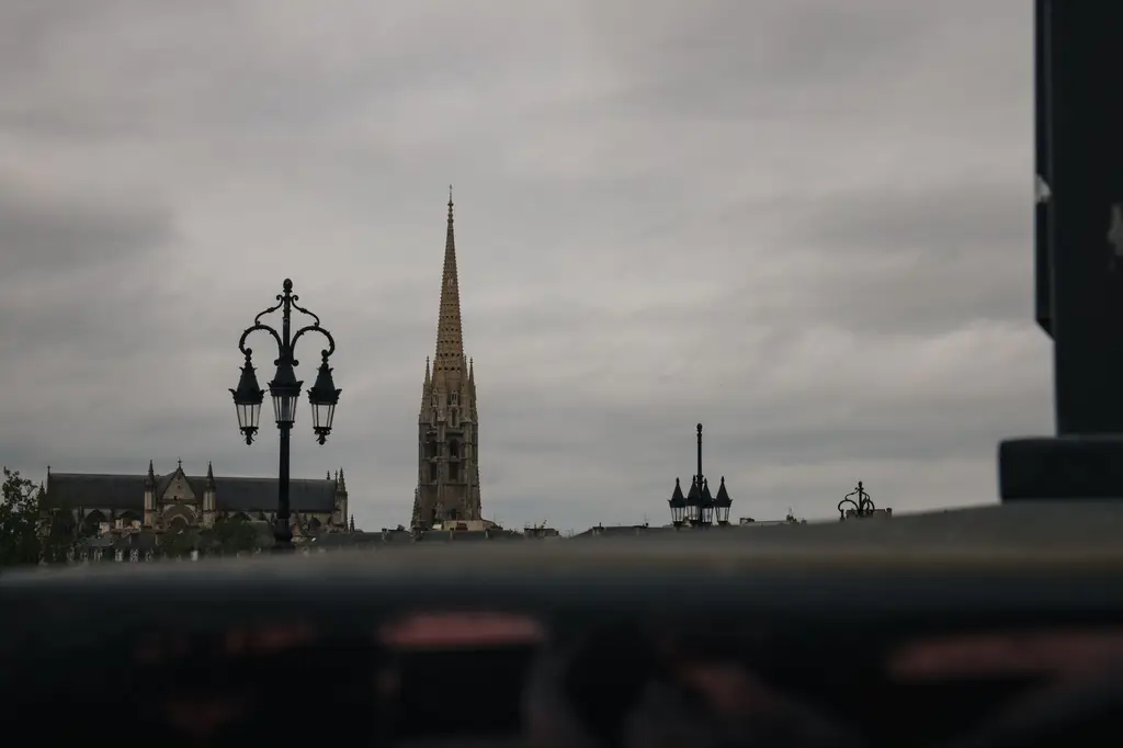 Bordeaux skyline featuring the iconic Gothic spire of Saint-Michel Basilica against a moody sky.