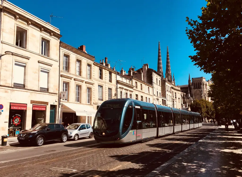 A sleek tram travels along a historic street in Bordeaux, featuring classic architecture and a cathedral.