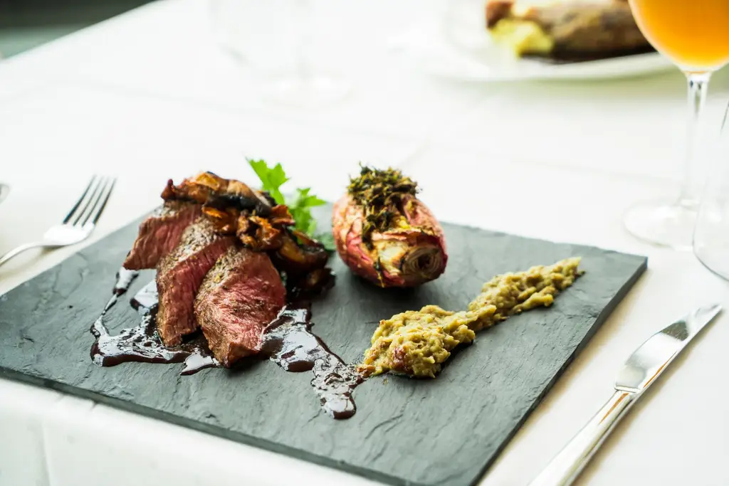 Deliciously plated steak with sauce and sides, served with wine on a clean white table.