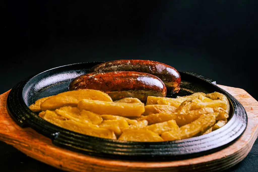 Rustic grilled sausage and potatoes served hot on a wooden sizzling plate, perfect for a hearty meal.