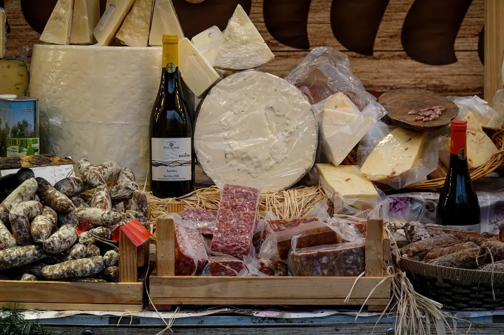 Assorted cheeses and sausages with wine bottles in a rustic market setting.