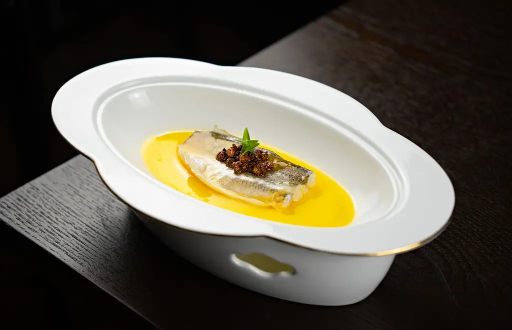 A sophisticated fish dish with a flavorful sauce, elegantly presented in a white dish, ideal for fine dining.