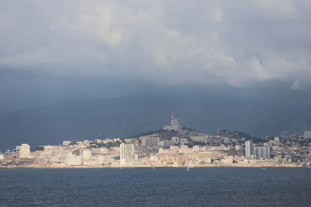 Panoramic view of Marseille skyline with Notre-Dame de la Garde under cloudy skies.