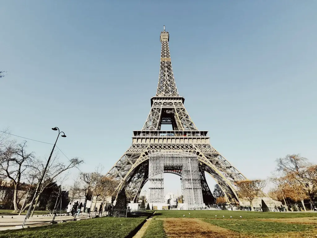 Low angle shot of the Eiffel Tower in Paris with blue sky and partial park view.