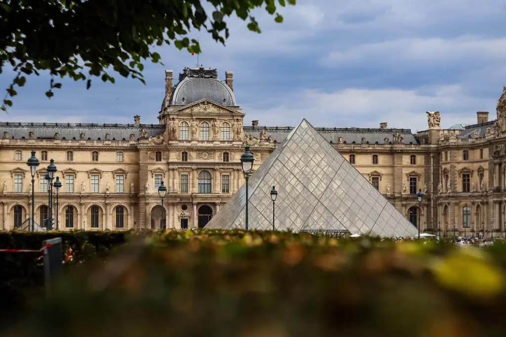 View of the Louvre Museum and glass pyramid in Paris, France during a cloudy day.