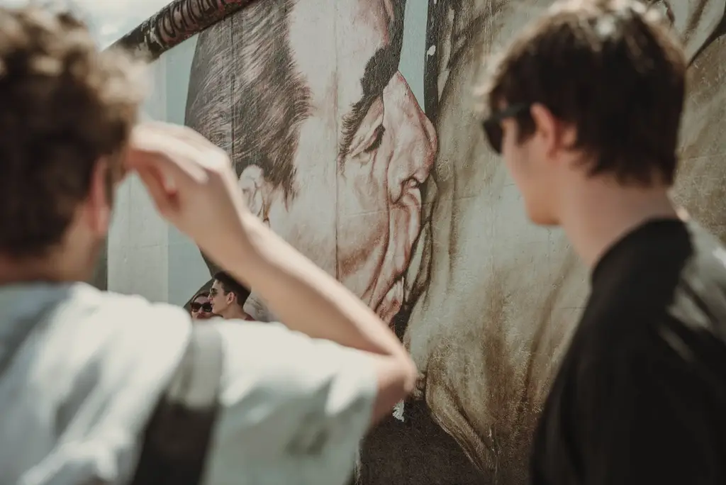 People observing the iconic Berlin Wall mural with close attention at the East Side Gallery.