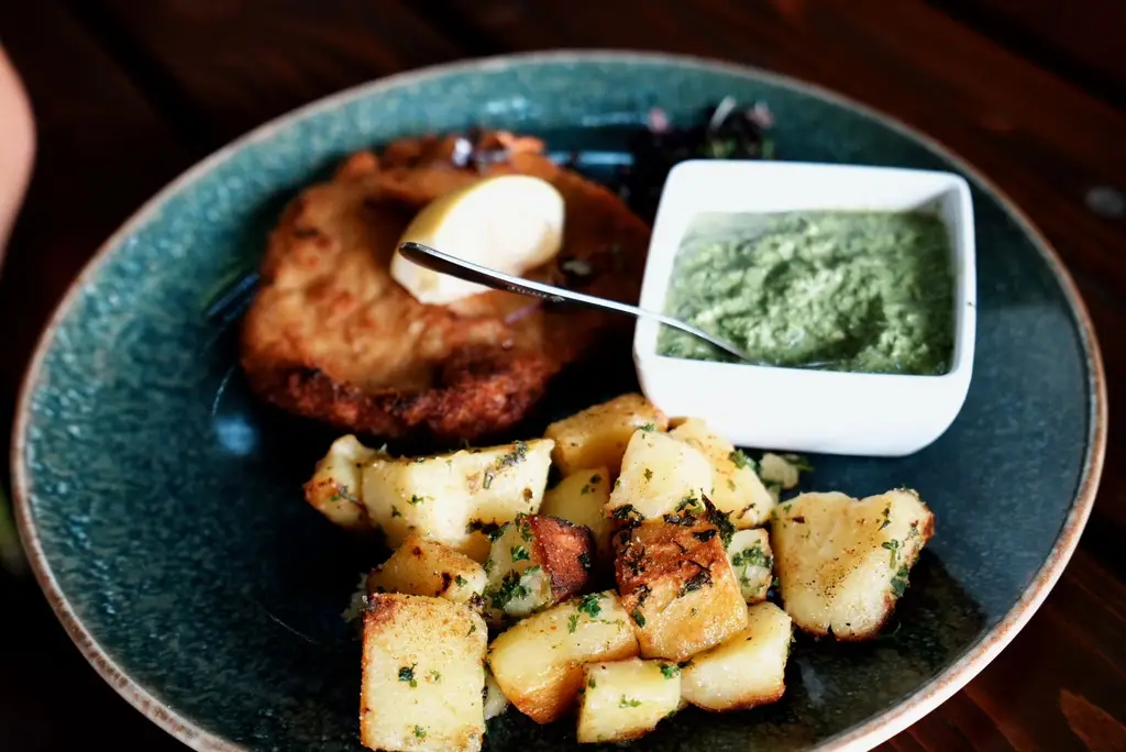 Plate of schnitzel, roasted potatoes, and green sauce, garnished with a lemon wedge.