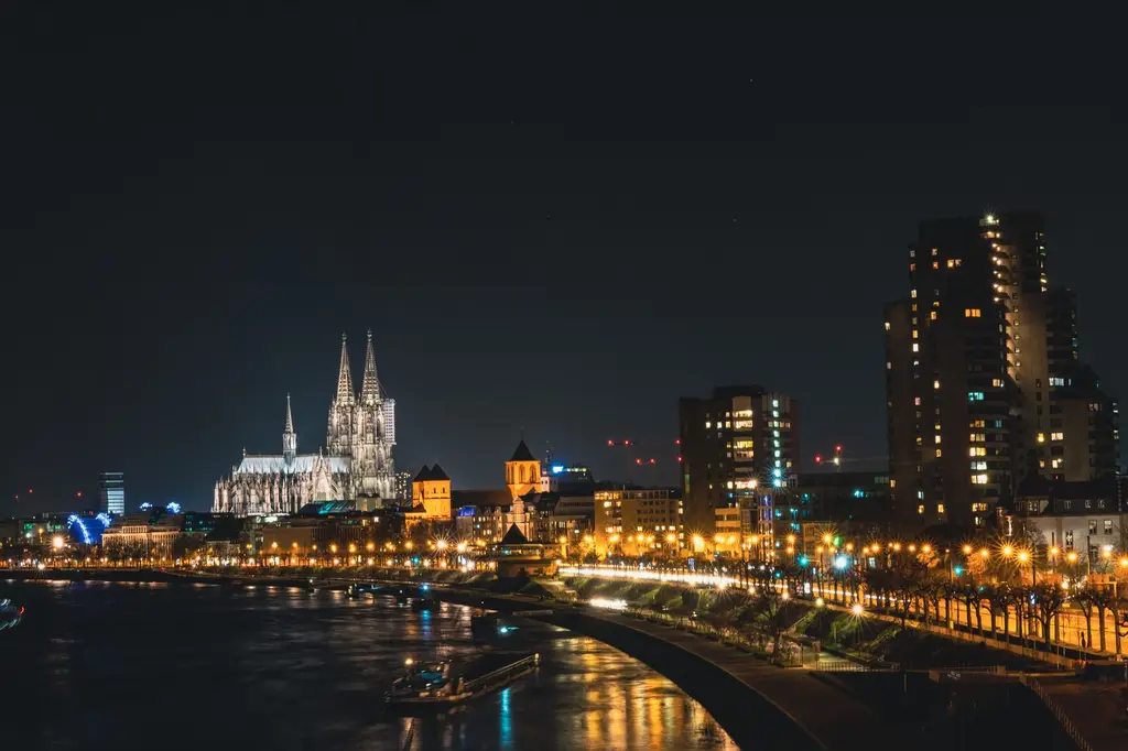 Dramatic night view of Cologne Cathedral and city skyline reflecting on the Rhine River, Germany.