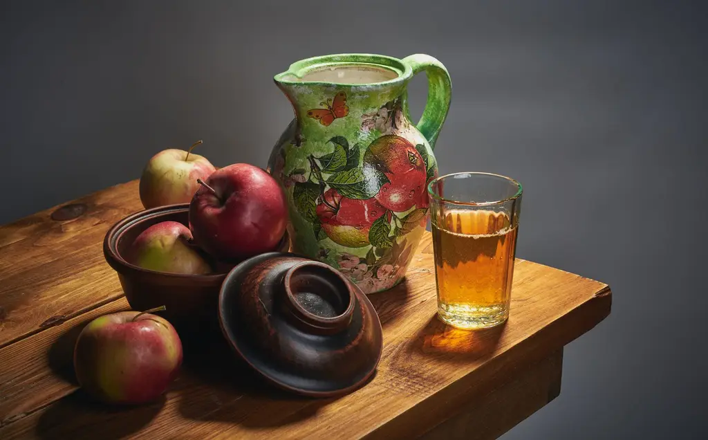 A colorful jug and fresh apples arranged on a wooden table in a classic still life setup.