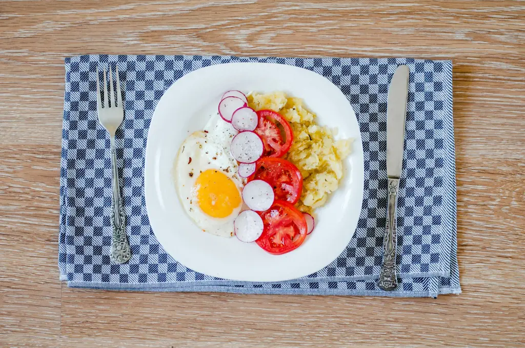 A delicious breakfast featuring fried eggs, tomatoes, radishes, and smashed potatoes.