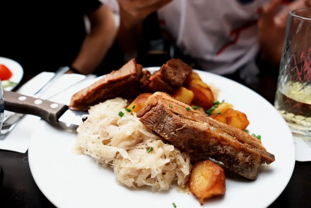 Plate of roast pork ribs, sauerkraut, and potatoes served in a cozy setting.