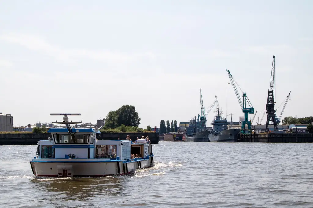A lively harbor scene in Hamburg with a boat sailing and construction cranes in the background.