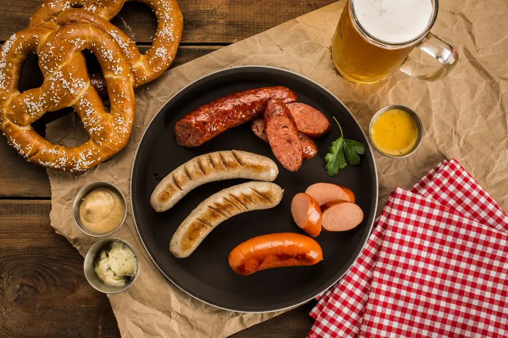A top view of a German-style meal with sausages, pretzels, dips, and beer on a rustic table.