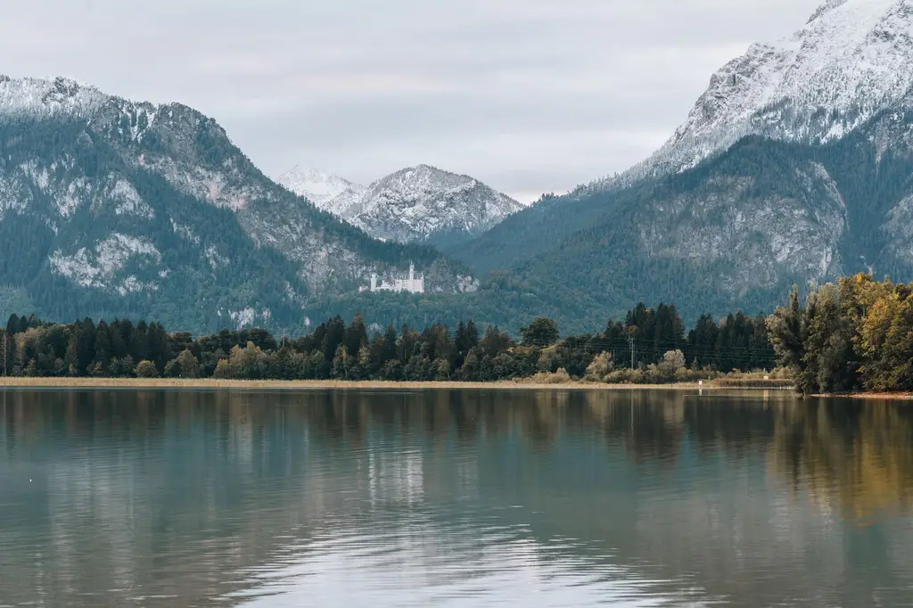 Tranquil landscape with Neuschwanstein Castle nestled in the Bavarian Alps, reflecting on the calm waters of Alpsee Lake.