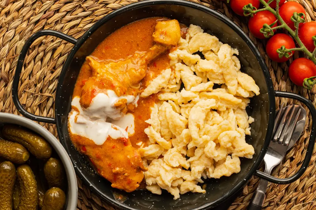 Indulge in flavorful chicken paprikash with noodles, pickles, and fresh tomatoes for a tasty meal.