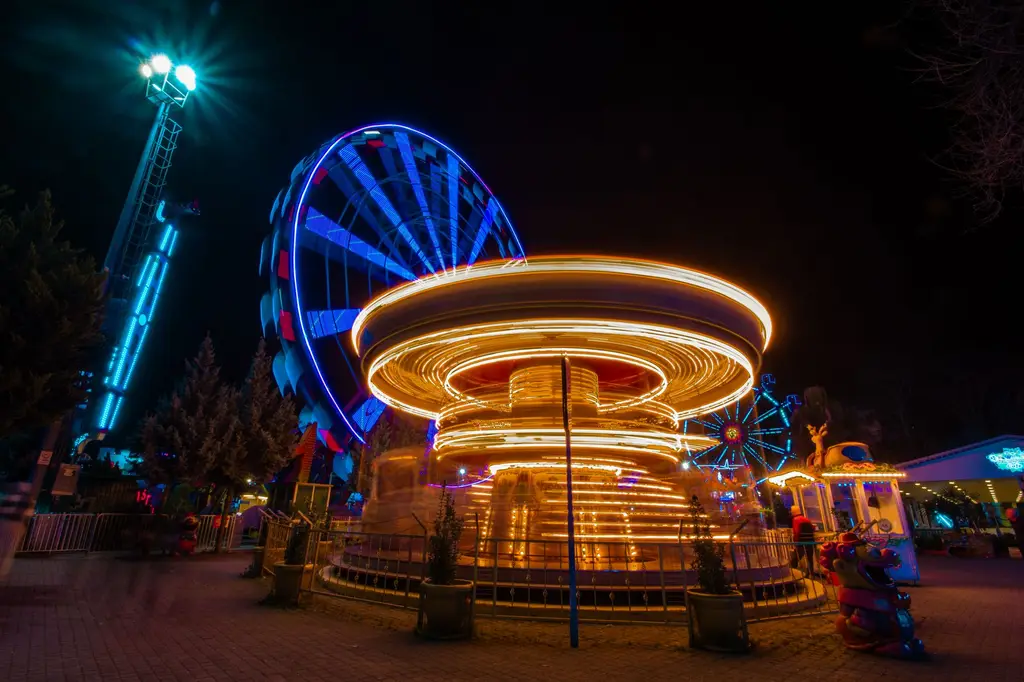 Colorful carousel and Ferris wheel light up a night-time amusement park in Bursa.