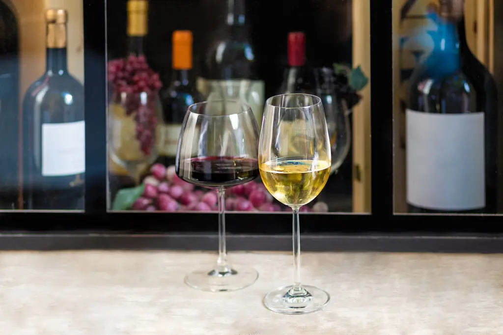 Close-up of red and white wine glasses with bottles and grapes in the background, perfect for wine tasting themes.