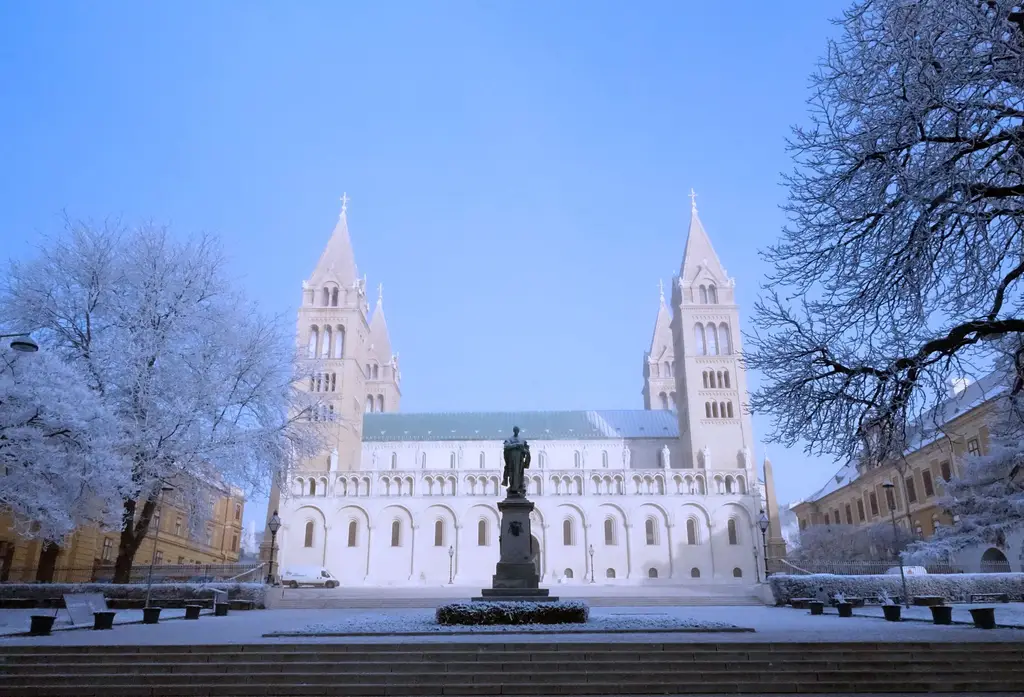 Snow-covered landscape of Pecs Cathedral with frosty trees and clear blue sky.