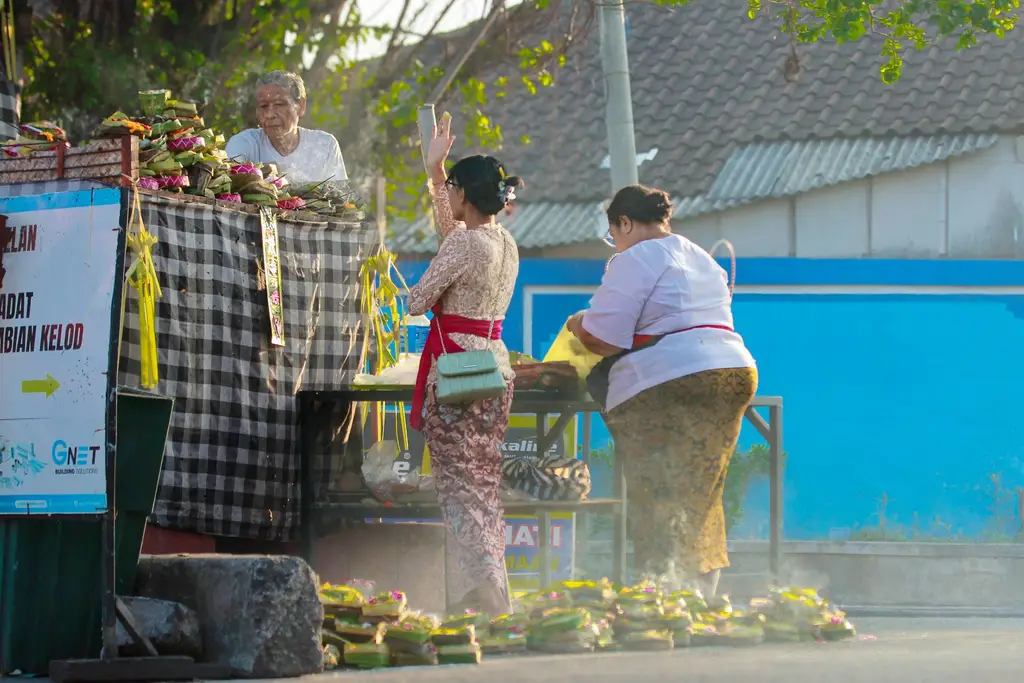 Balinese women in traditional attire preparing offerings at a Denpasar market during a sunny day.