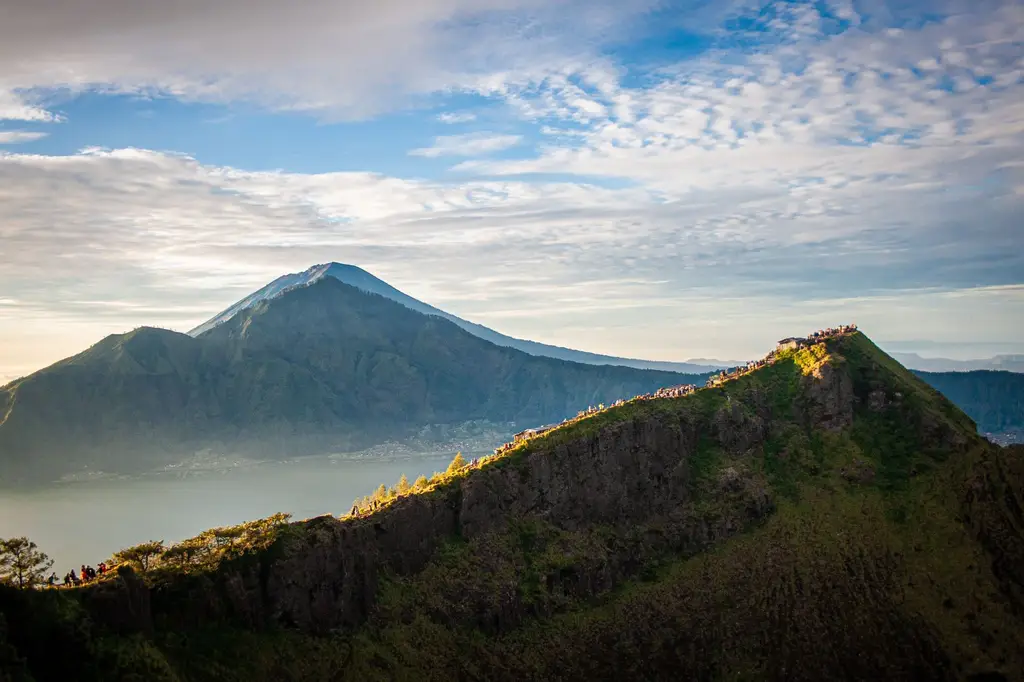 Breathtaking view of Mount Batur with tourists enjoying the sunrise in Bali's lush landscape.
