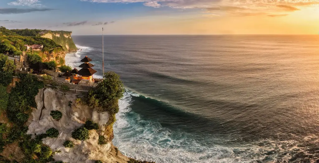 A breathtaking aerial view of Uluwatu Temple perched on cliffs overlooking the ocean at sunset in Bali, Indonesia.