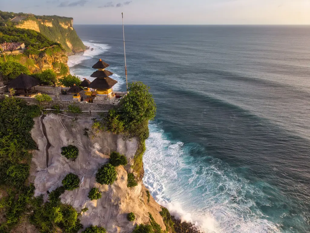 Aerial view of Uluwatu Temple perched on a cliff in Bali, Indonesia, at sunset.