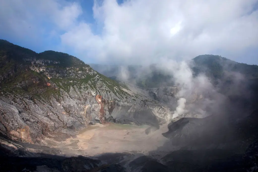 Aerial shot of the Tangkuban Perahu volcanic crater releasing steam under a cloudy sky.