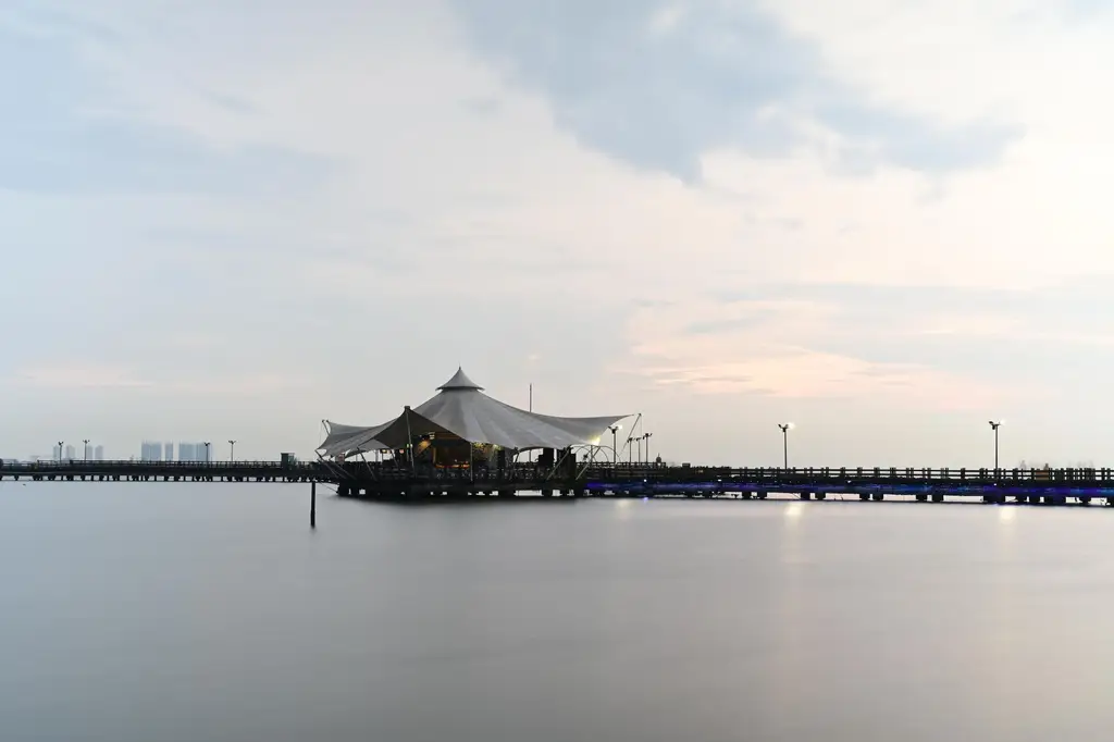 Peaceful dusk view of a pier and pavilion on Jakarta's waterfront, with calm waters.