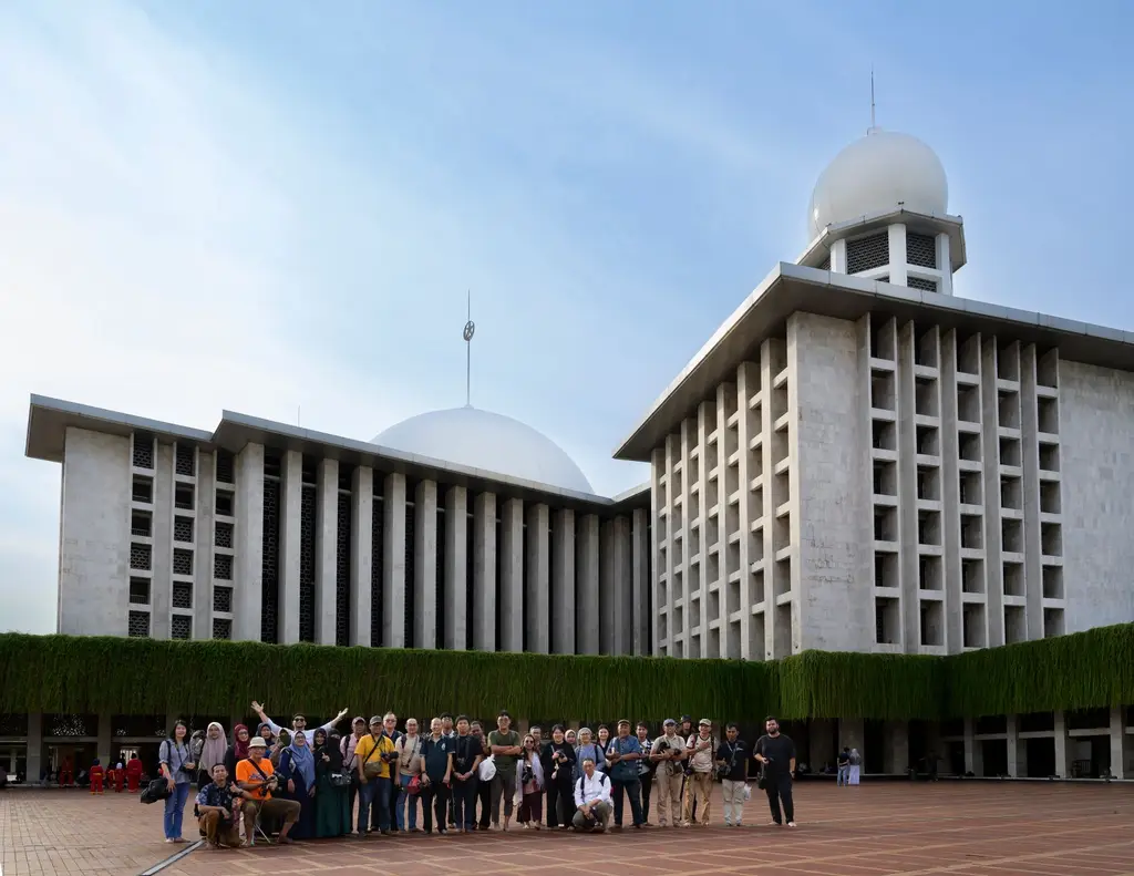 A diverse group of people pose outside the iconic Istiqlal Mosque in Jakarta, showcasing its unique architecture.