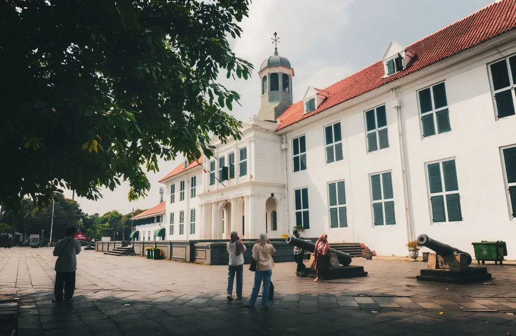 View of a historical colonial building in Jakarta's Kota Tua with tourists and cannons in the foreground.