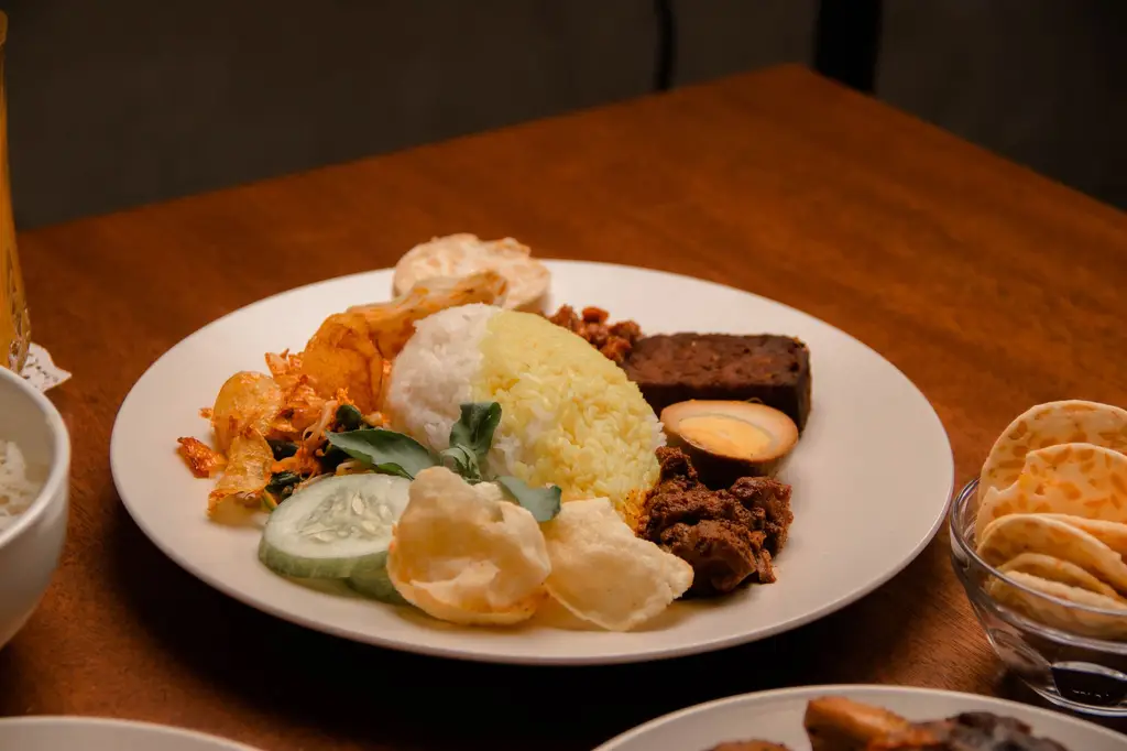 Plate of Nasi Padang with rice, egg, vegetables, and meat on a wooden table.